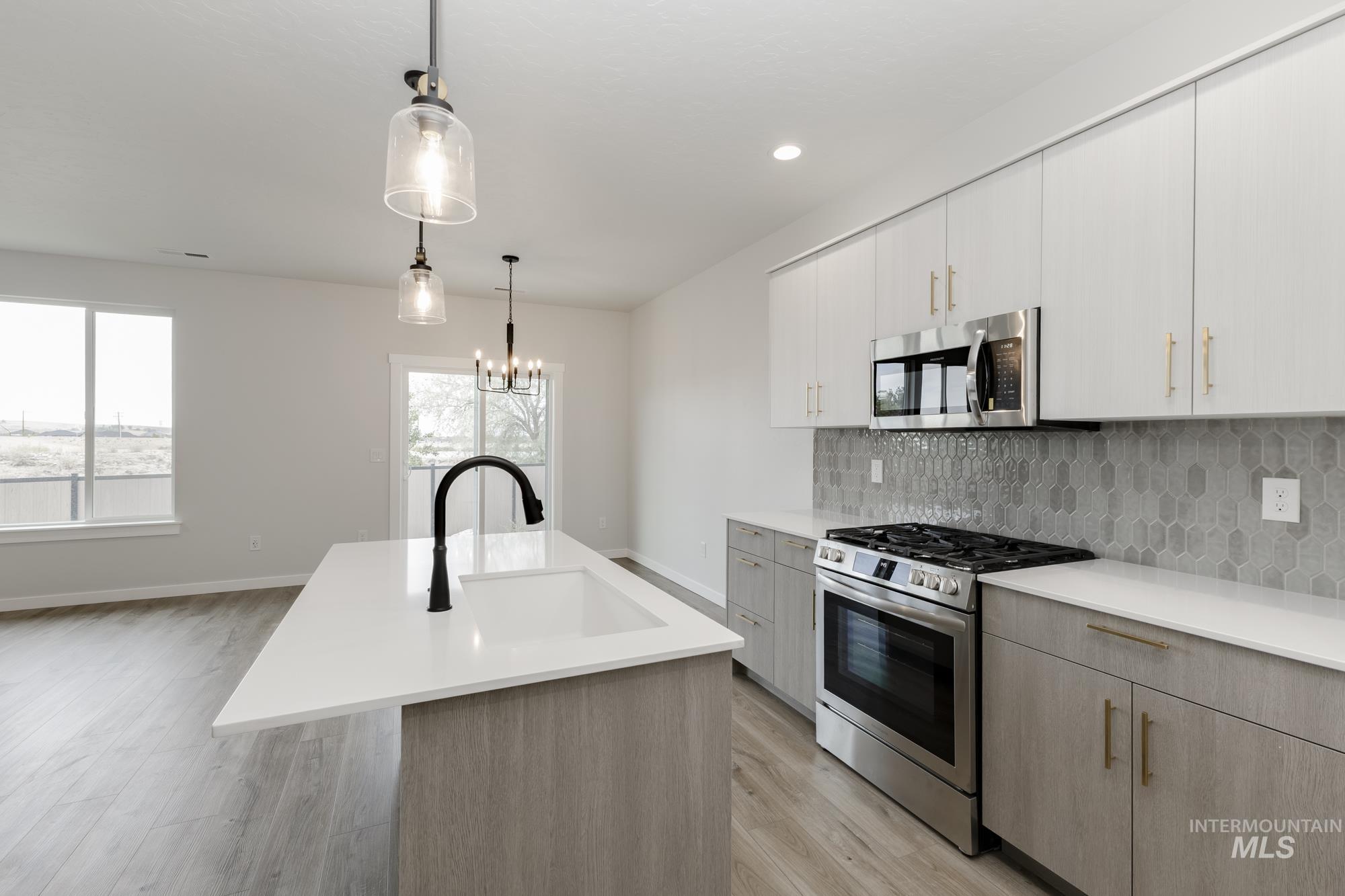 Kitchen featuring stainless steel appliances, backsplash, pendant lighting, a kitchen island with sink, and light wood finished floors