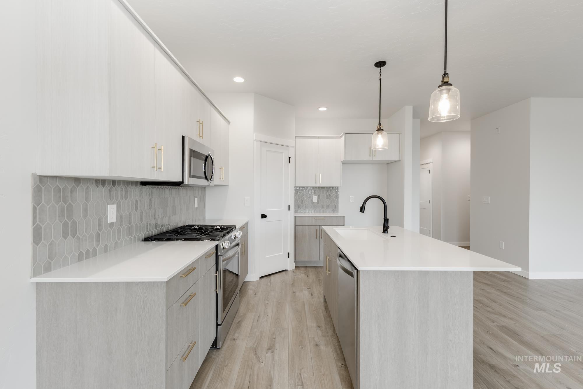 Kitchen featuring stainless steel appliances, modern cabinets, decorative light fixtures, light wood-style flooring, and a center island with sink