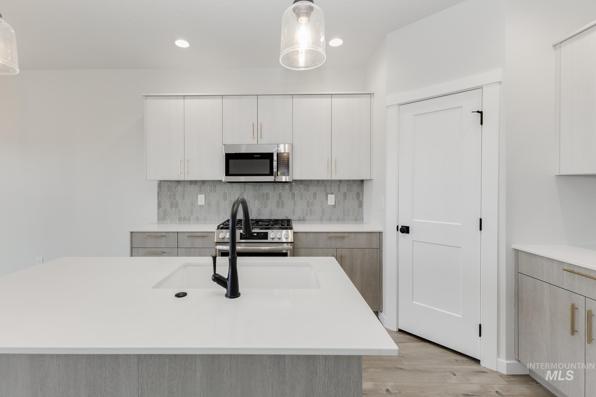 Kitchen featuring appliances with stainless steel finishes, decorative backsplash, light wood-style floors, hanging light fixtures, and recessed lighting