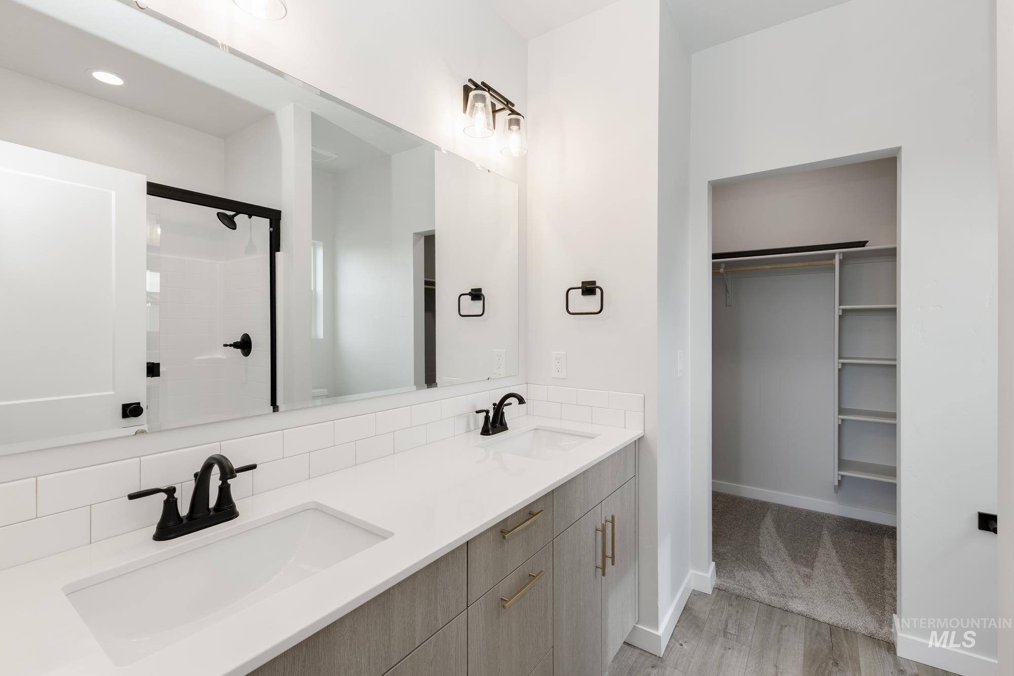 Bathroom with a walk in closet, light wood-style floors, a shower stall, and double vanity