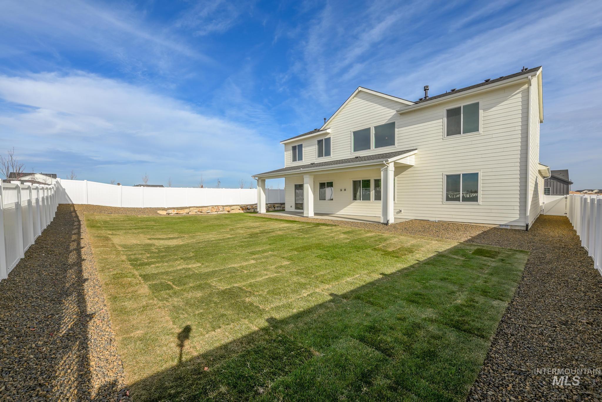 Expansive backyard featuring a new sod lawn, gravel border, full white vinyl fencing, and a covered concrete patio