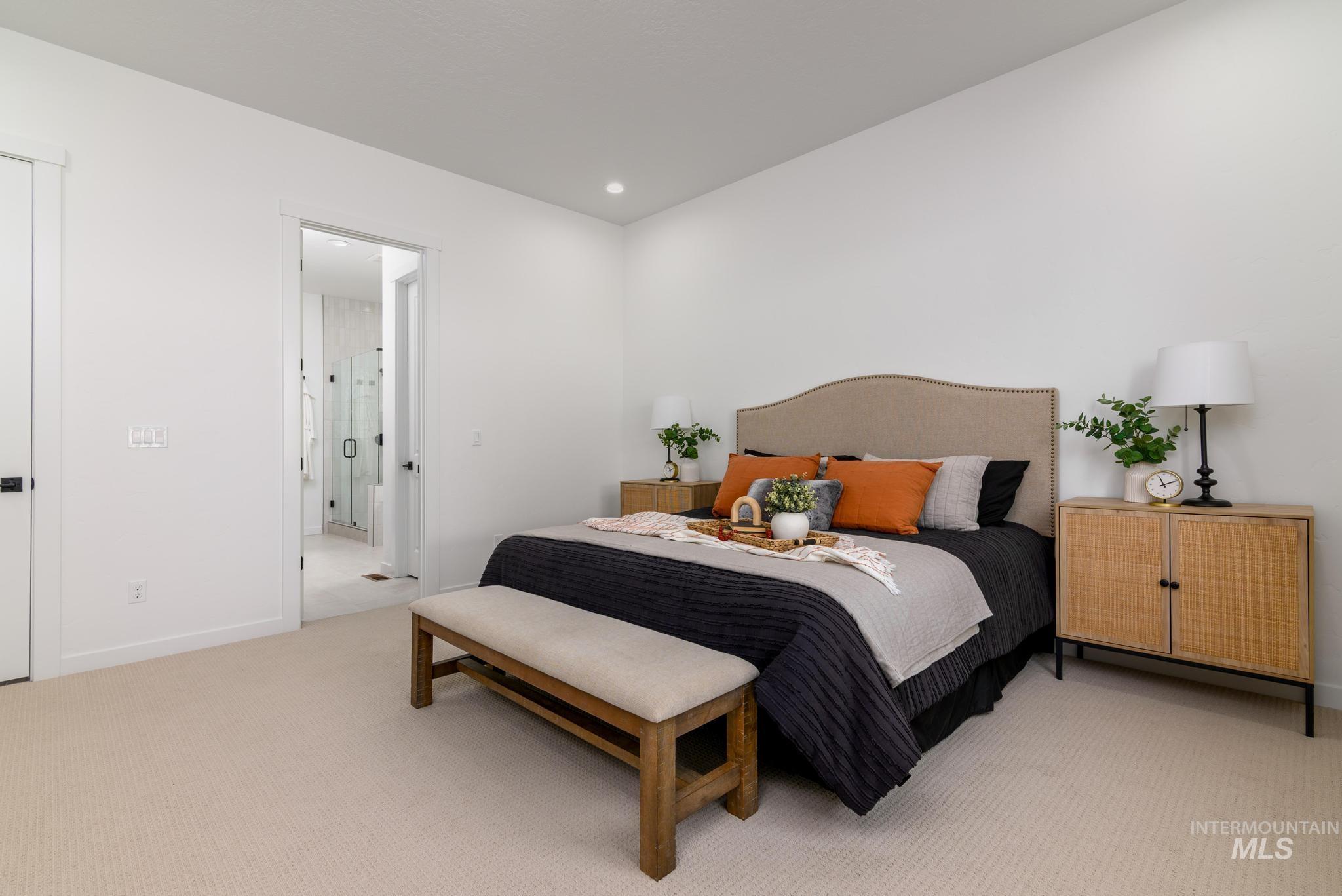 Carpeted room with a textile-upholstered headboard, recessed lighting, and a doorway opening to a bathroom with a glass-enclosed shower