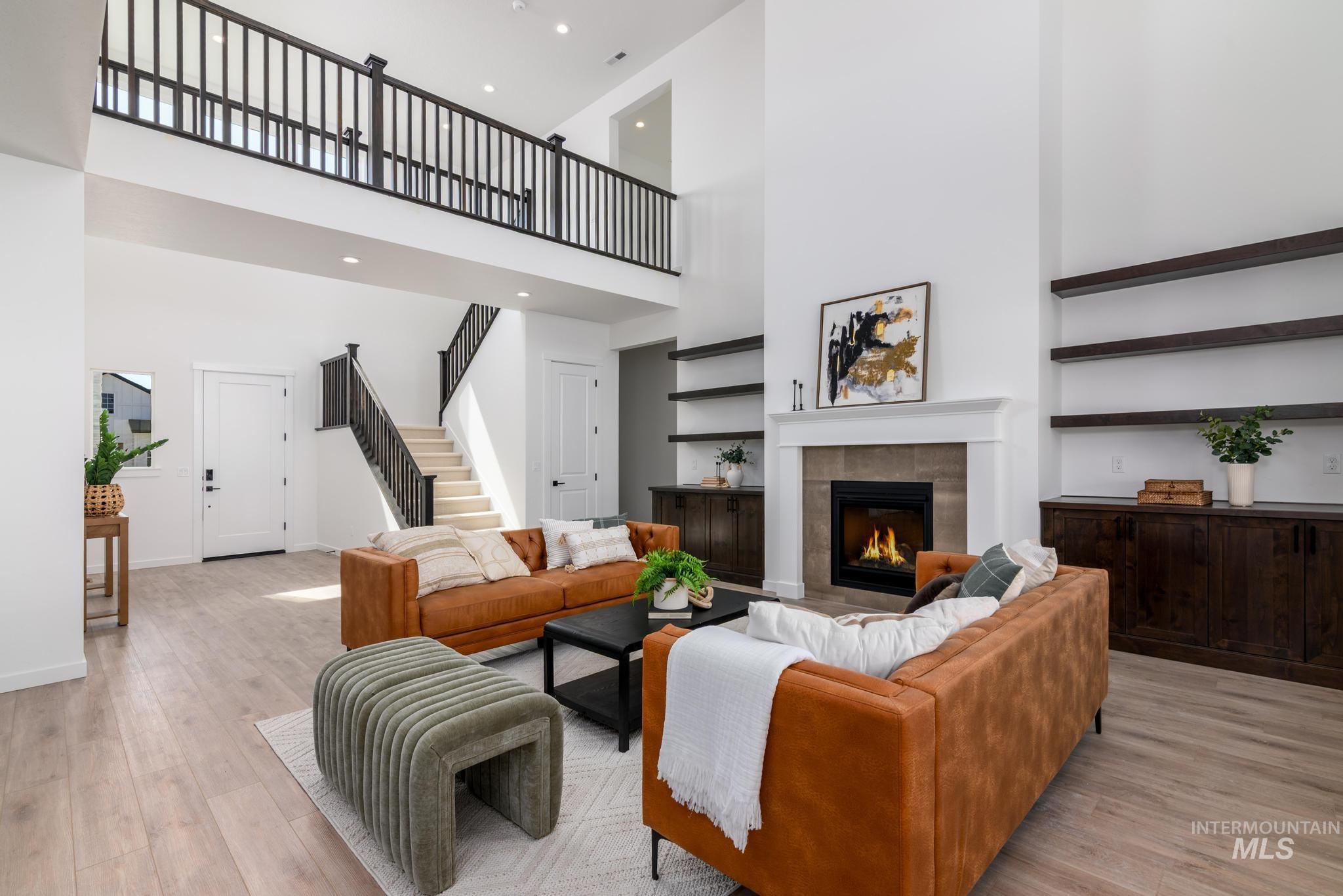 Spacious living area featuring a two-story ceiling, light wood-finish flooring, and a fireplace with a stone surround and white mantel
