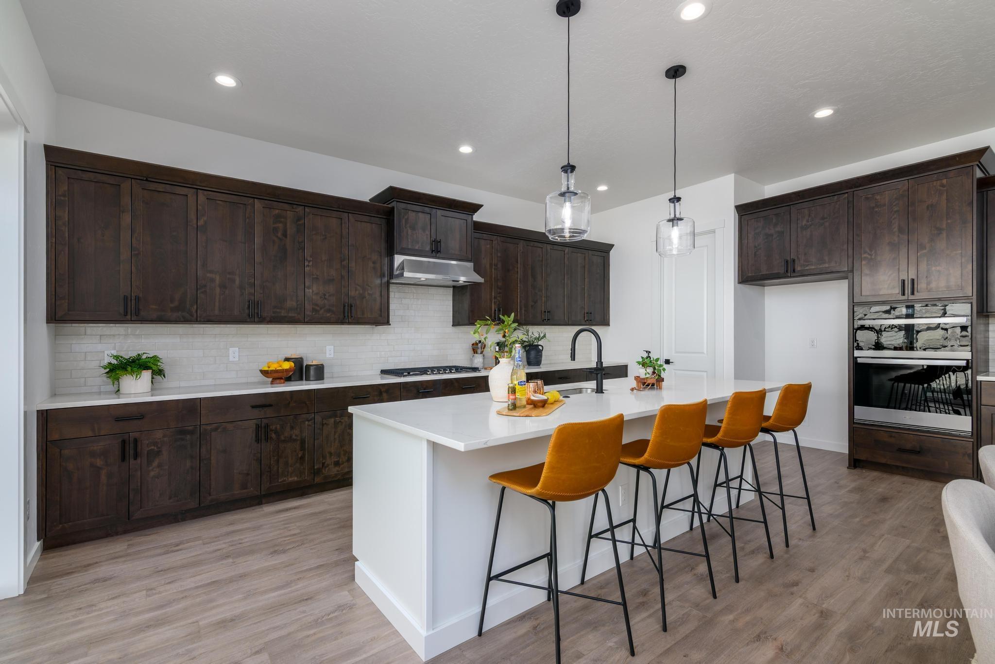 Open-concept kitchen featuring an expansive island with white countertop, dark wood cabinetry, a subway tile backsplash, and light wood-finish flooring