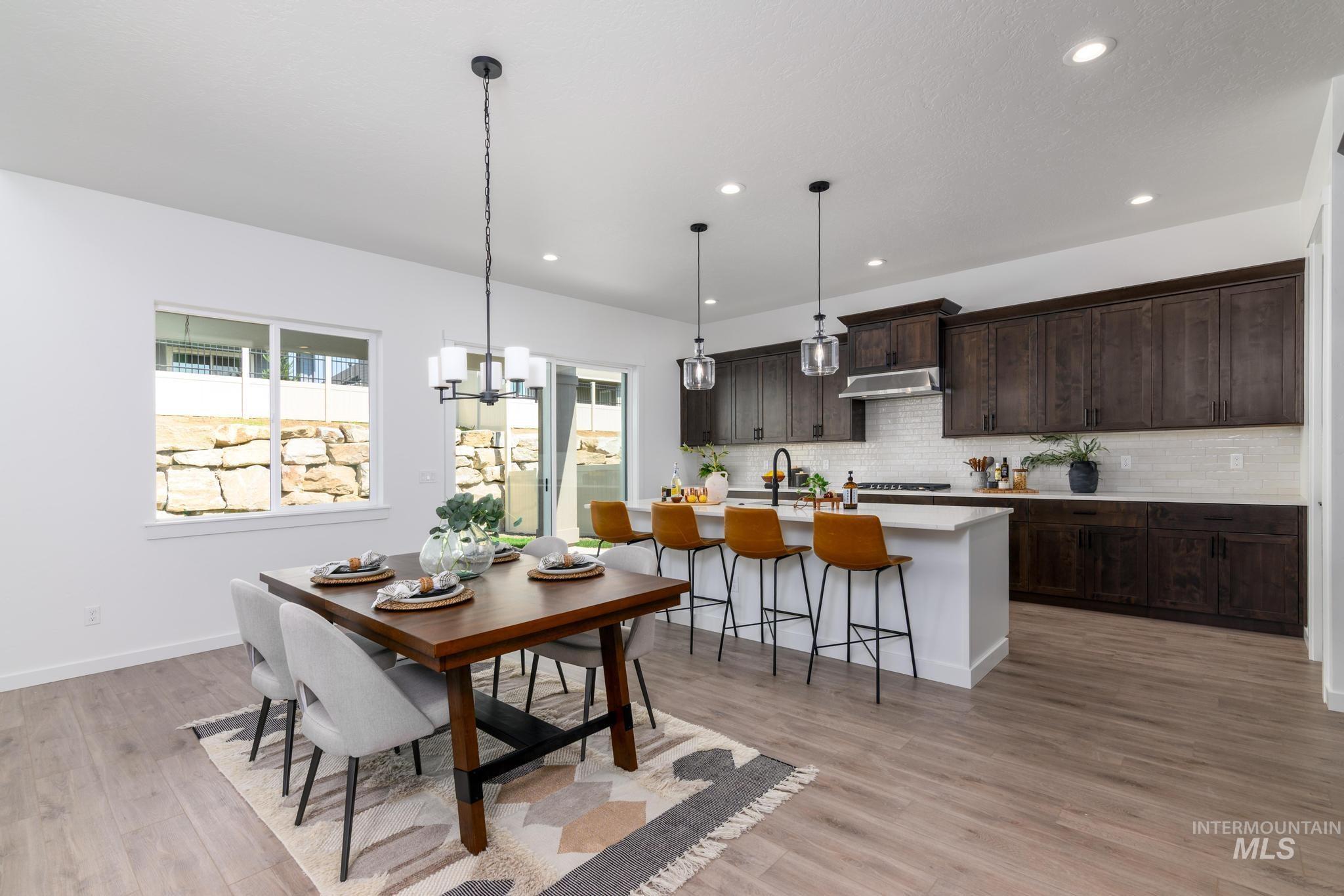 Open-concept interior featuring light wood-finish flooring, a contemporary dining area with chandelier, and a kitchen island with pendant lighting