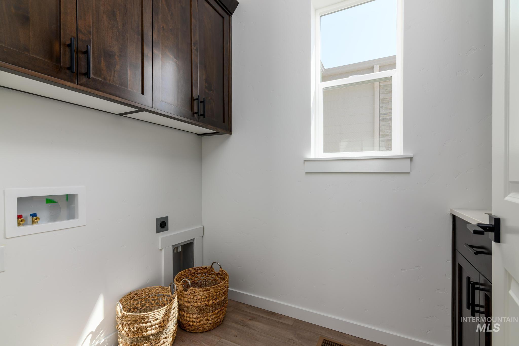 Laundry area featuring dark wood-finish cabinetry with black hardware, a single window, and light wood-finish flooring