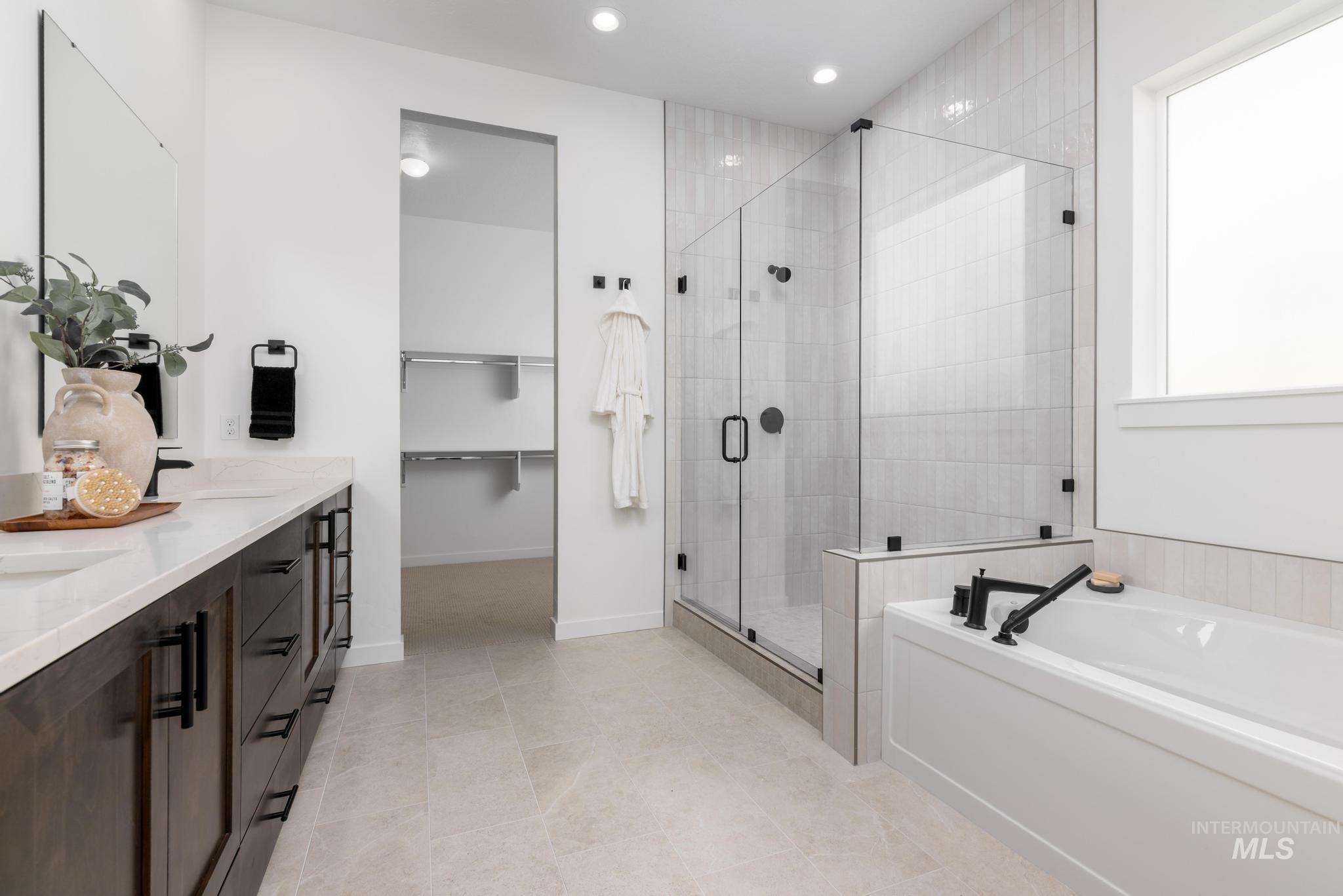 Spacious bathroom featuring a dual vanity with light-colored countertops, a glass-enclosed shower with tiled walls, a separate soaking tub, and neutral-toned flooring