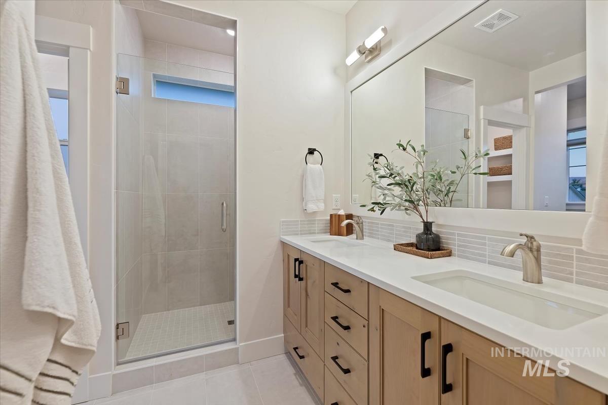 Bathroom featuring double vanity, light tile patterned floors, tasteful backsplash, and a stall shower