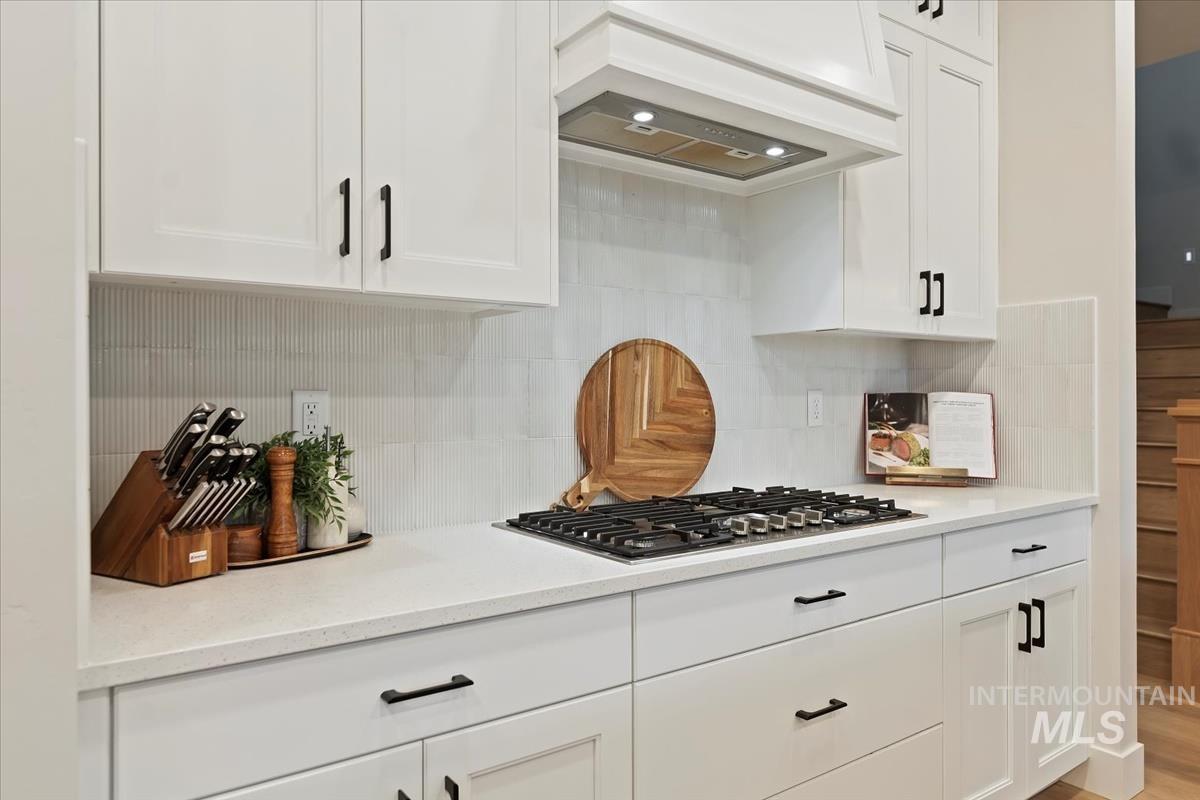 Kitchen featuring white cabinetry, custom exhaust hood, light stone countertops, and light wood finished floors