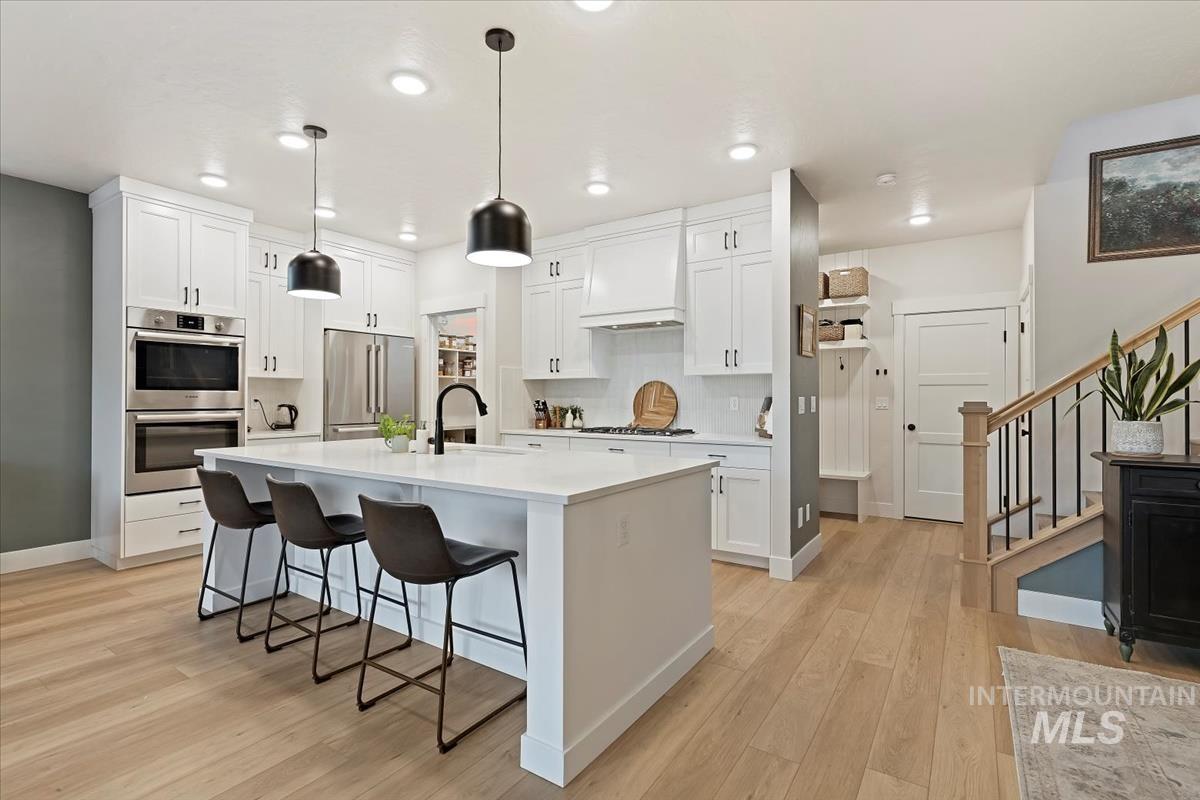 Kitchen with an island with sink, stainless steel appliances, decorative backsplash, a breakfast bar, and light wood finished floors