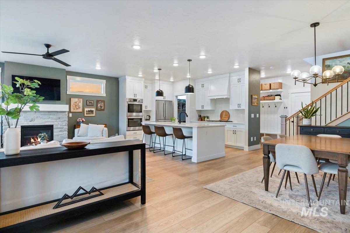 Living area featuring stairs, light wood-style flooring, a fireplace, ceiling fan, and a chandelier