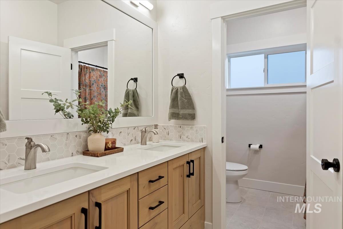 Full bath with backsplash, double vanity, and light tile patterned floors