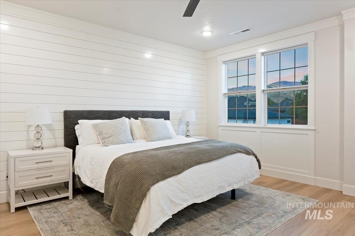 Bedroom with light wood-style floors, a ceiling fan, crown molding, and wooden walls