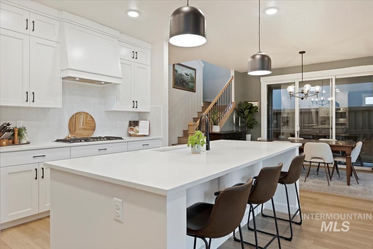 Kitchen featuring light wood-type flooring, hanging light fixtures, white cabinets, tasteful backsplash, and recessed lighting