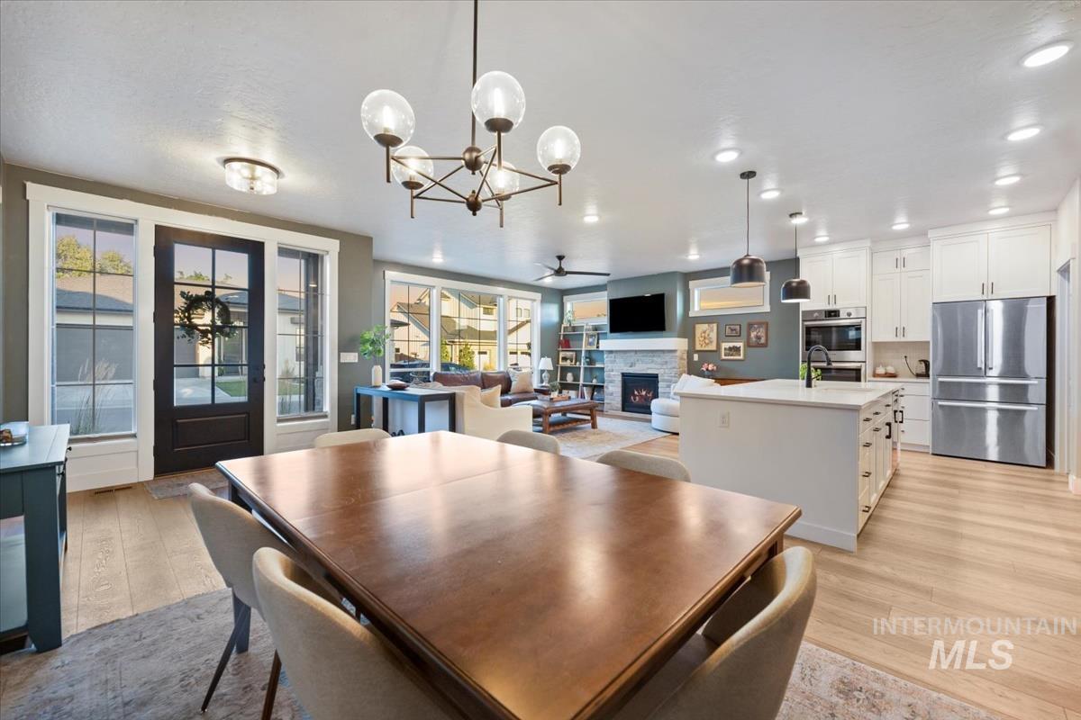 Dining area featuring a stone fireplace, light wood-style floors, a chandelier, a ceiling fan, and recessed lighting