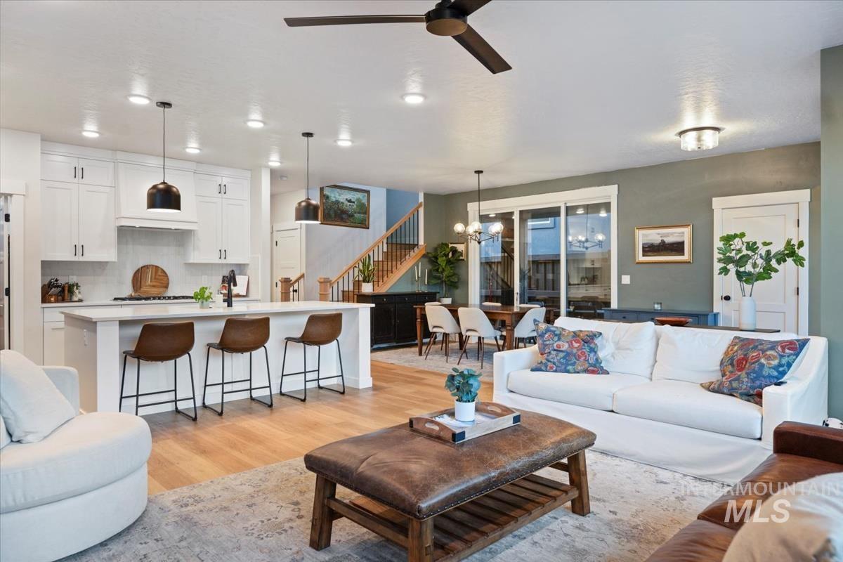 Living room featuring a chandelier, light wood finished floors, stairs, and ceiling fan