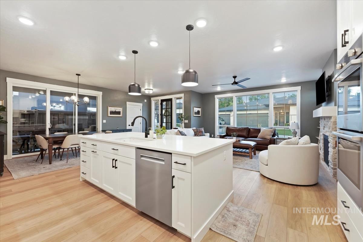 Kitchen featuring white cabinets, a ceiling fan, hanging light fixtures, appliances with stainless steel finishes, and light wood finished floors