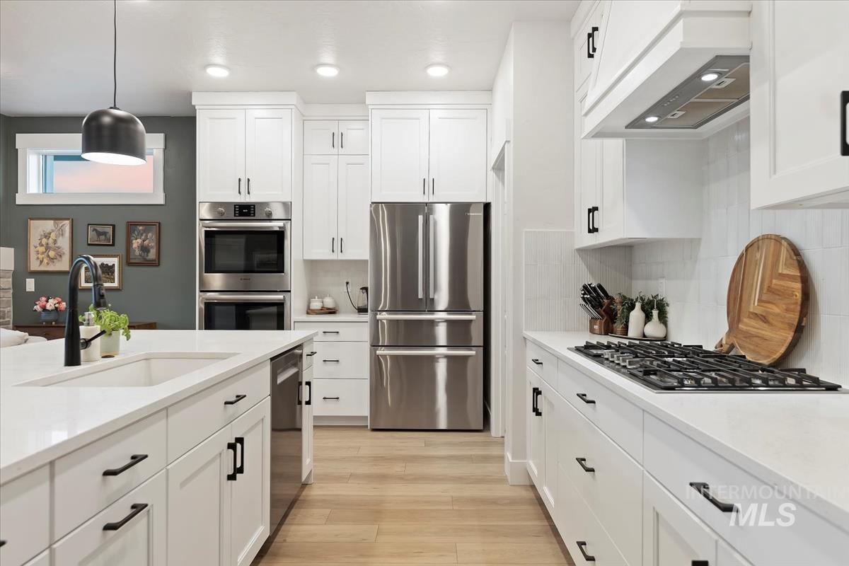 Kitchen featuring white cabinets, stainless steel appliances, custom range hood, pendant lighting, and recessed lighting