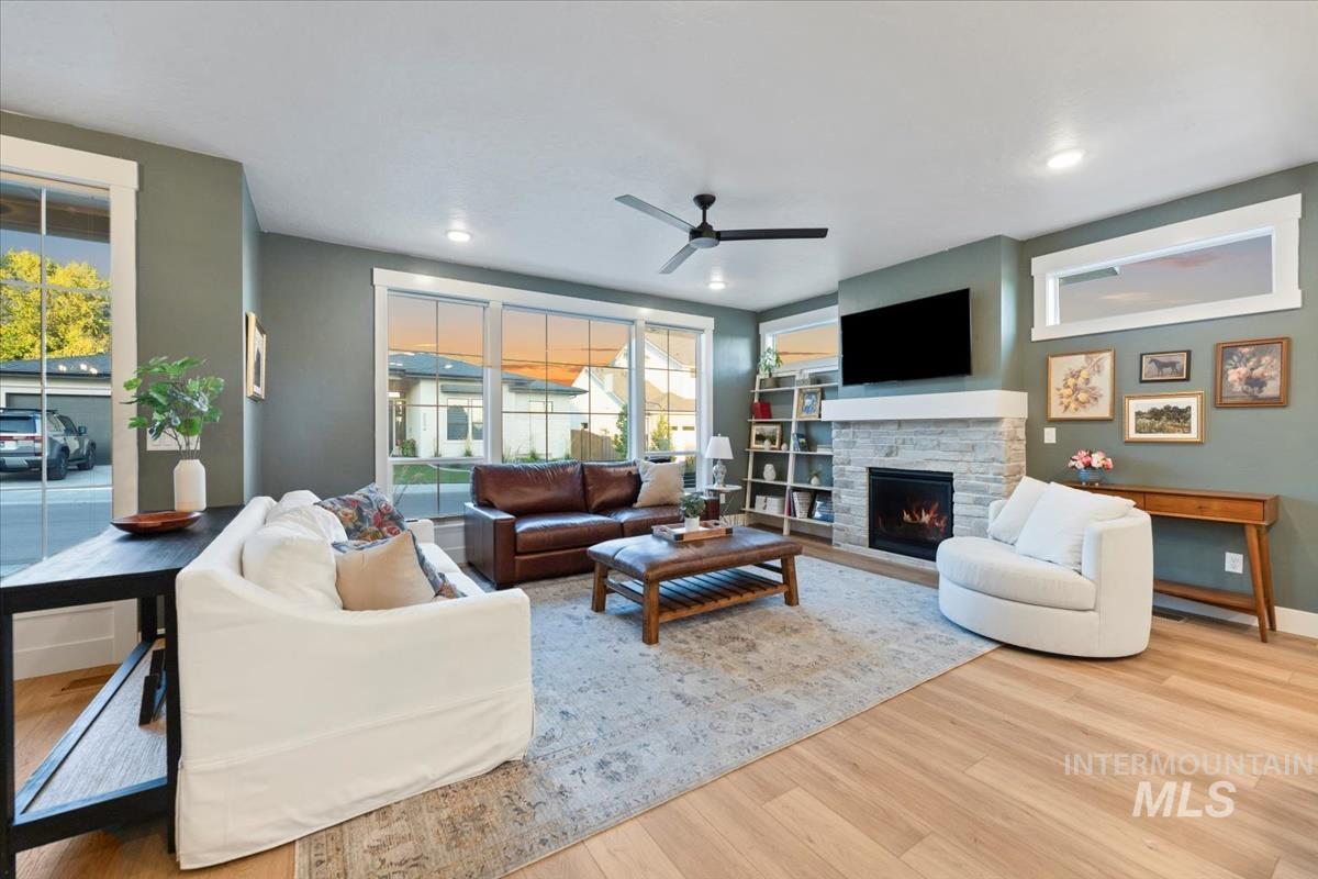 Living room with a stone fireplace, a ceiling fan, and wood finished floors