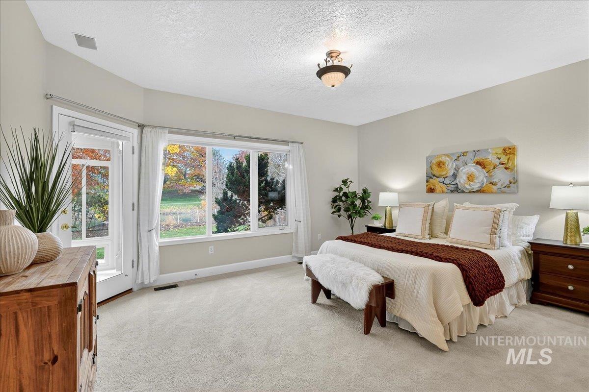 Bedroom with a textured ceiling, light colored carpet, and access to exterior
