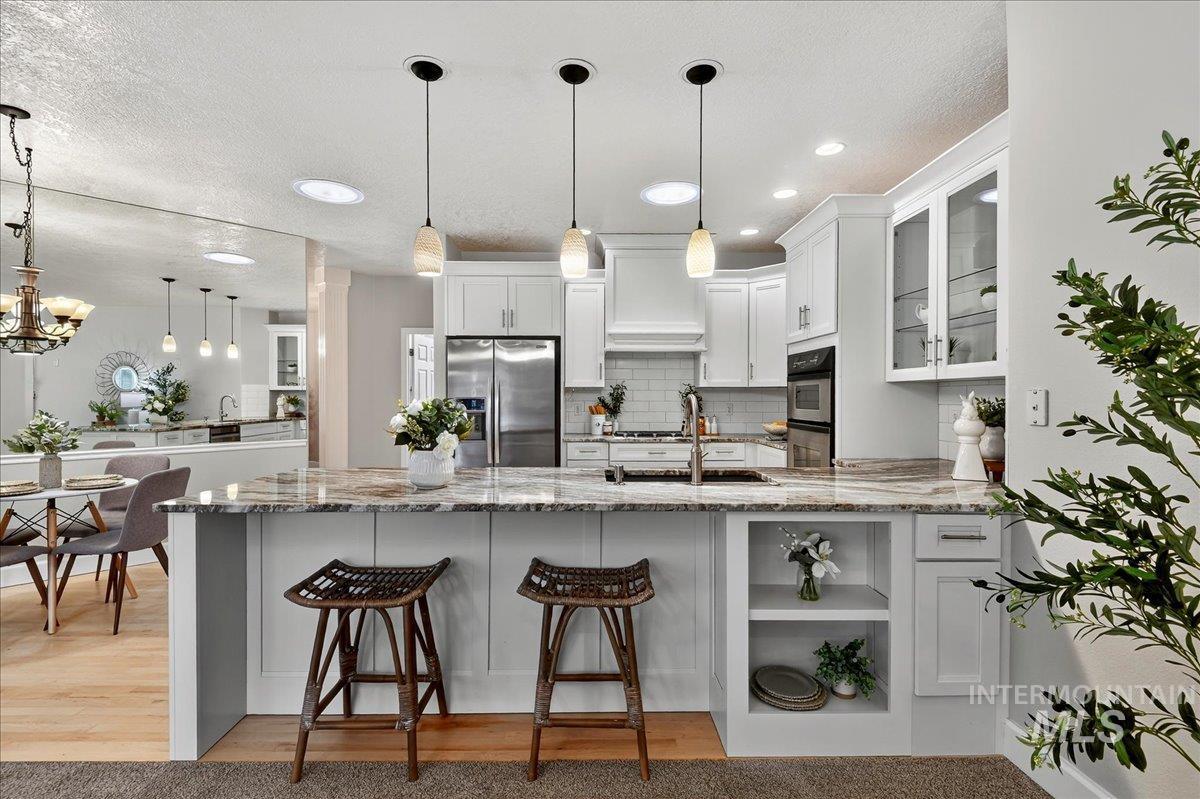 Kitchen with decorative light fixtures, white cabinetry, light stone countertops, backsplash, and a peninsula