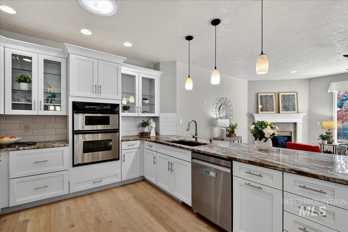 Kitchen with dark stone counters, appliances with stainless steel finishes, white cabinets, hanging light fixtures, and a tiled fireplace