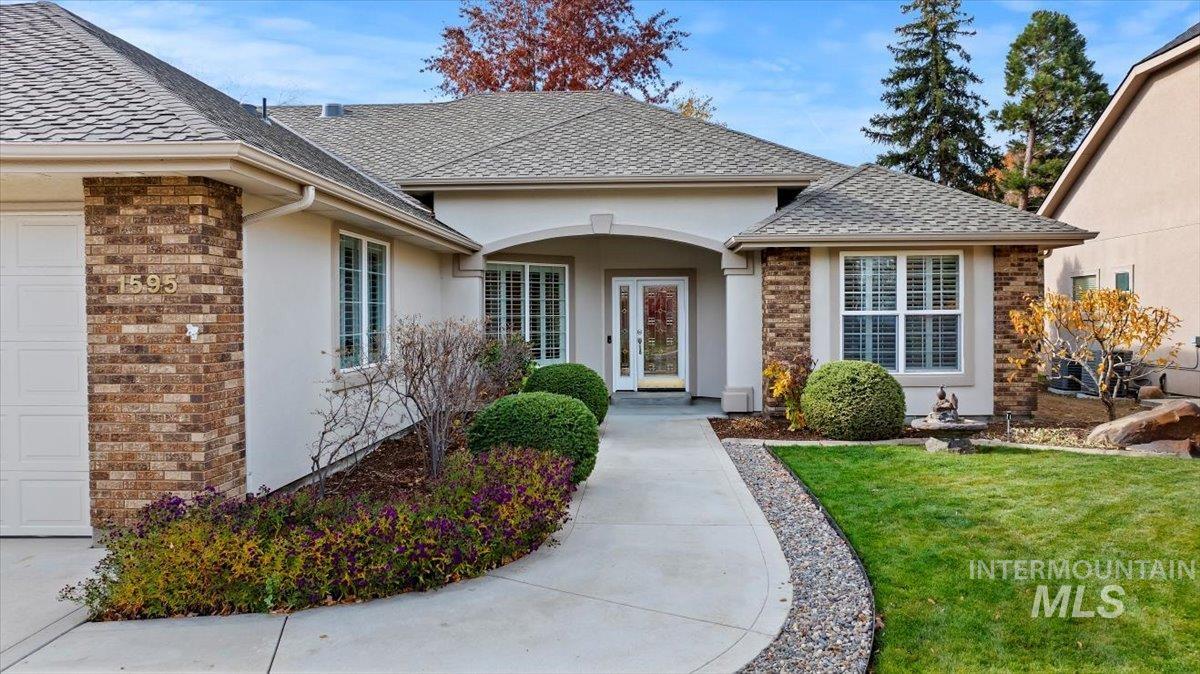 View of exterior entry with a yard, stucco siding, and a shingled roof