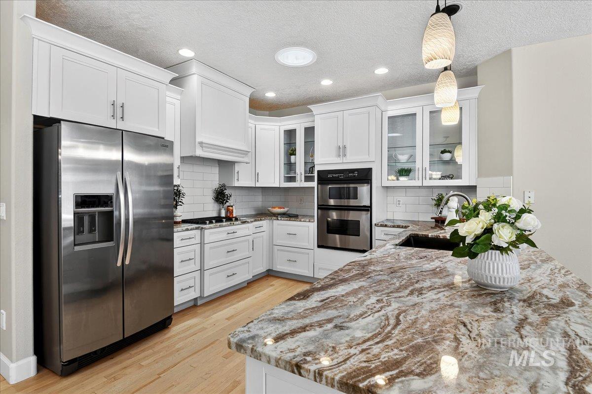 Kitchen with stainless steel appliances, light stone countertops, decorative light fixtures, a textured ceiling, and white cabinetry