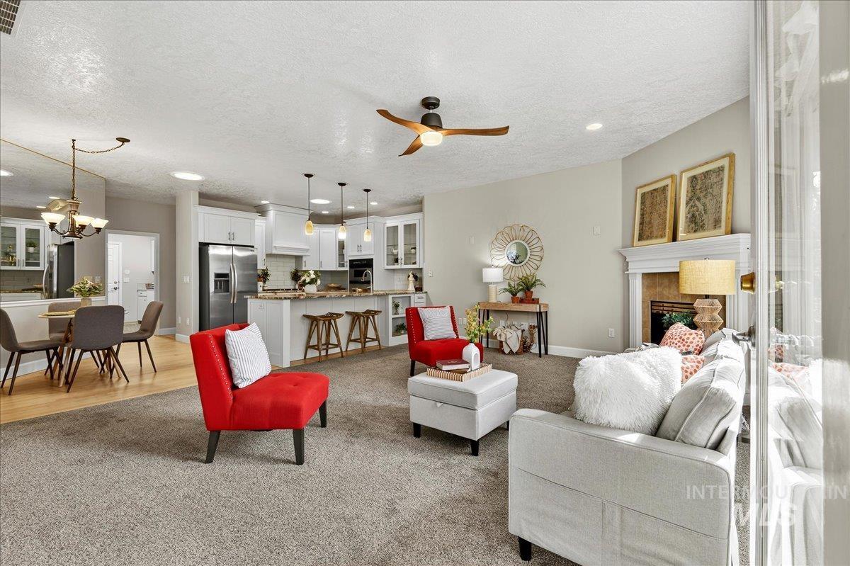 Carpeted living area featuring a textured ceiling, ceiling fan, recessed lighting, a fireplace, and a chandelier