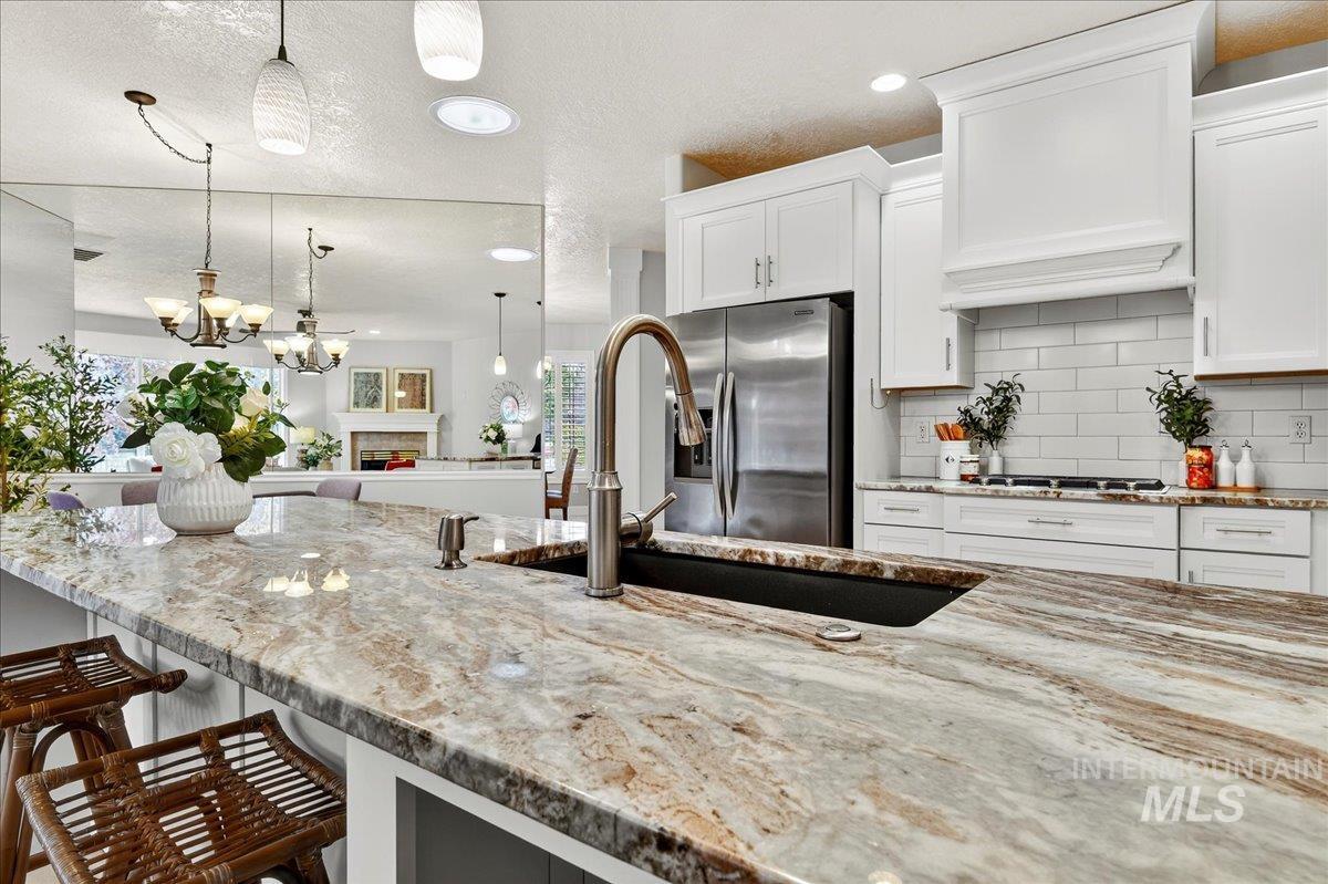 Kitchen featuring light stone counters, white cabinetry, a textured ceiling, and backsplash