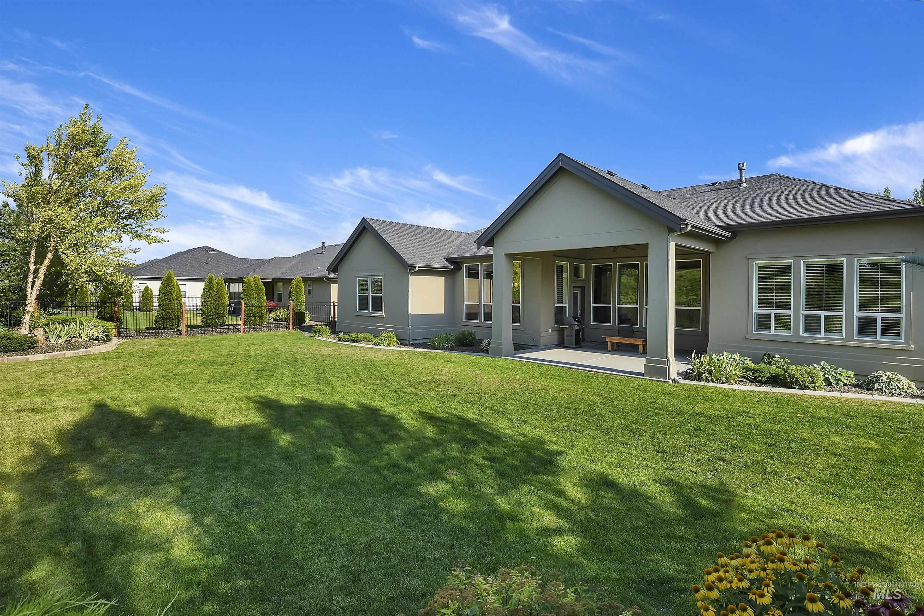 Expansive backyard featuring a manicured lawn, established landscaping, and a covered patio