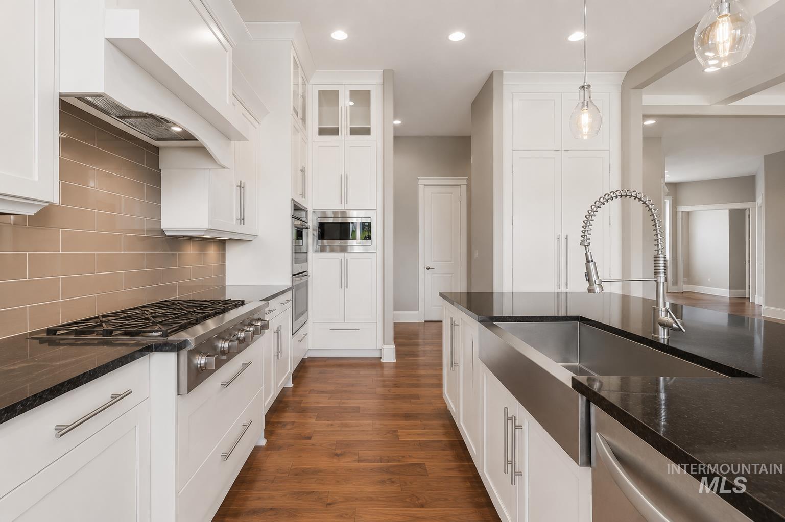 Gourmet kitchen featuring a stainless steel gas range, built-in double ovens, white cabinetry, dark countertops, and wood-finish flooring