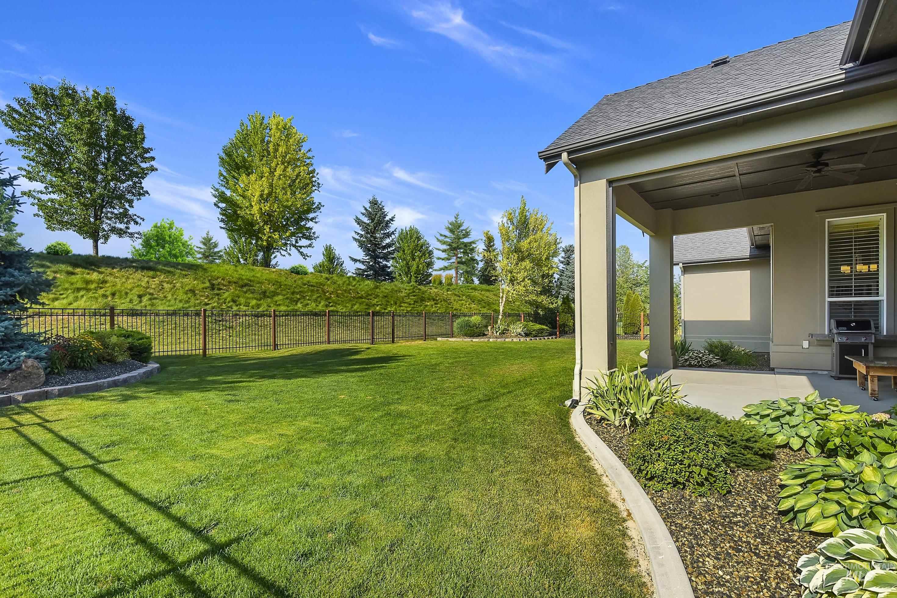 Expansive backyard featuring a manicured lawn, established landscaping, and a covered patio with a ceiling fan