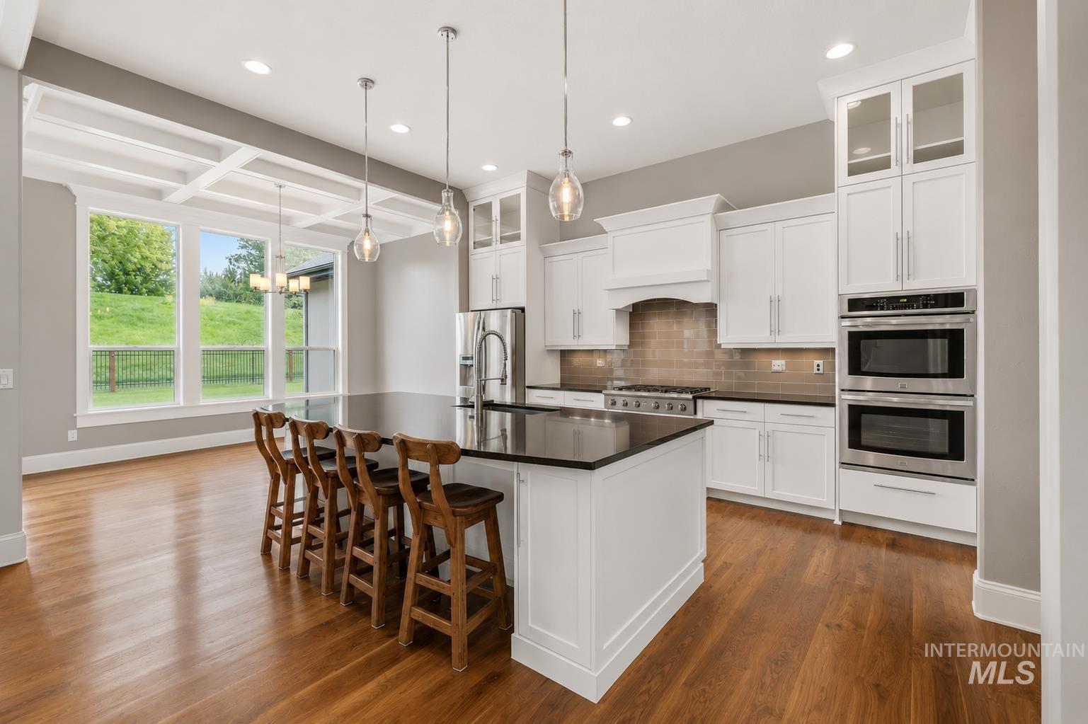 Gourmet kitchen featuring a large central island with seating, white shaker cabinetry, stainless steel appliances, and wood-finish flooring