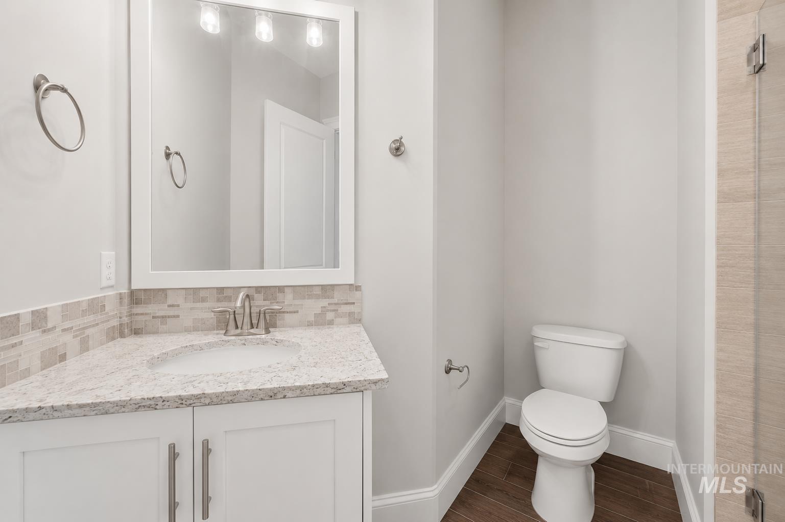 White vanity with a granite-finish countertop, integrated sink, and mosaic tile backsplash