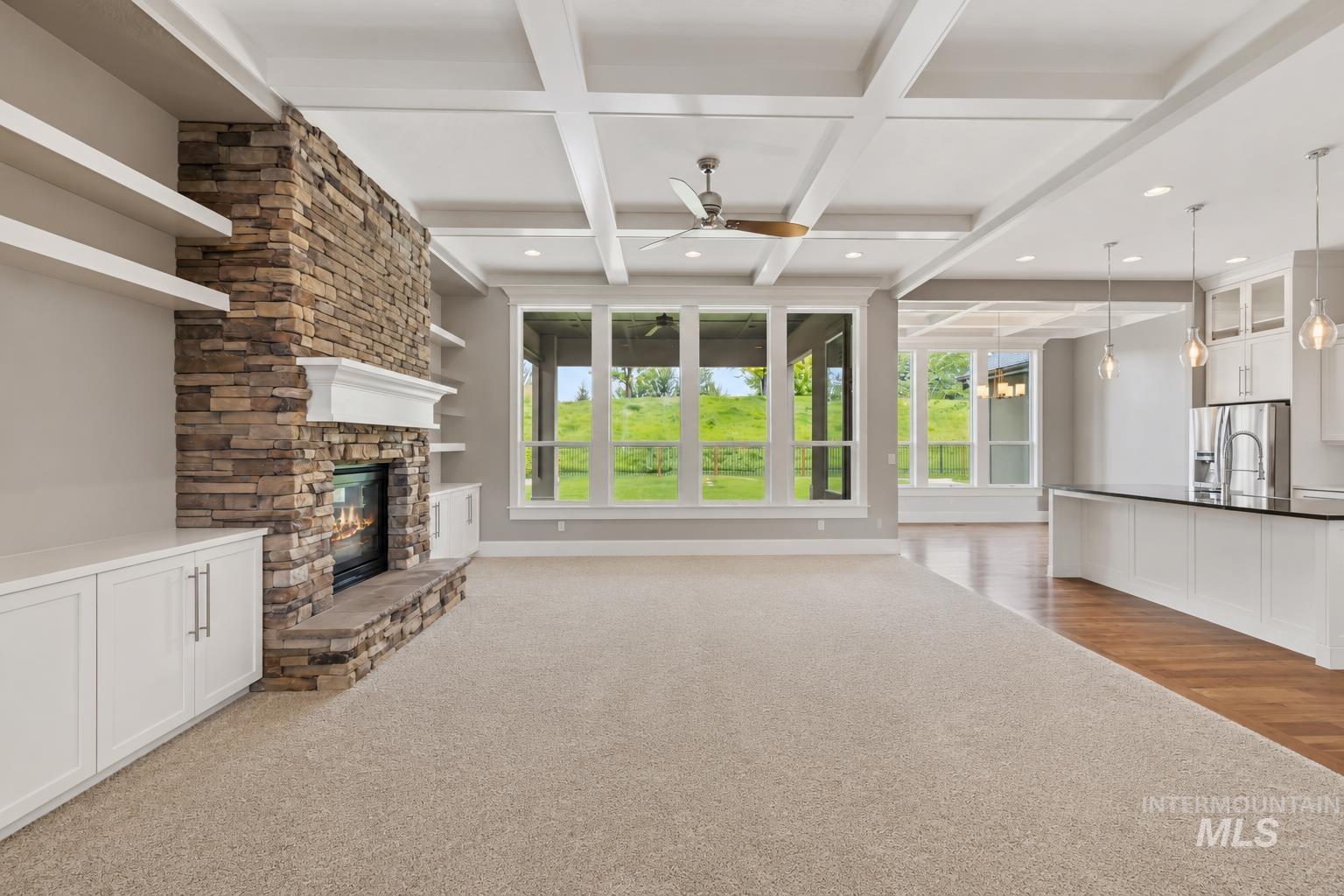 Spacious living area featuring a stacked stone fireplace with a white mantel, built-in shelving, and white cabinetry