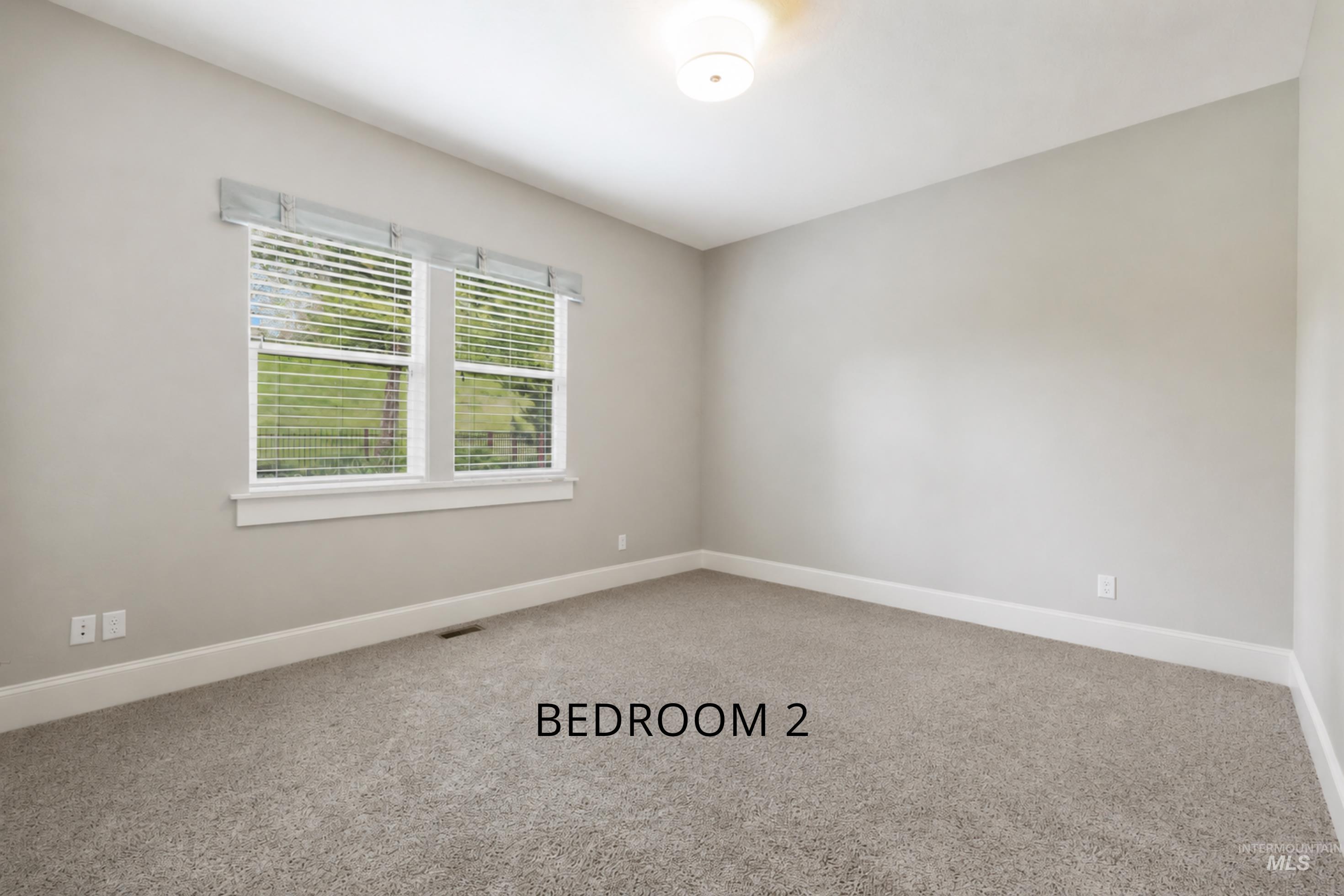 Light-filled room featuring neutral wall paint, gray carpet, white baseboards, and a double window with blinds and a fabric valance