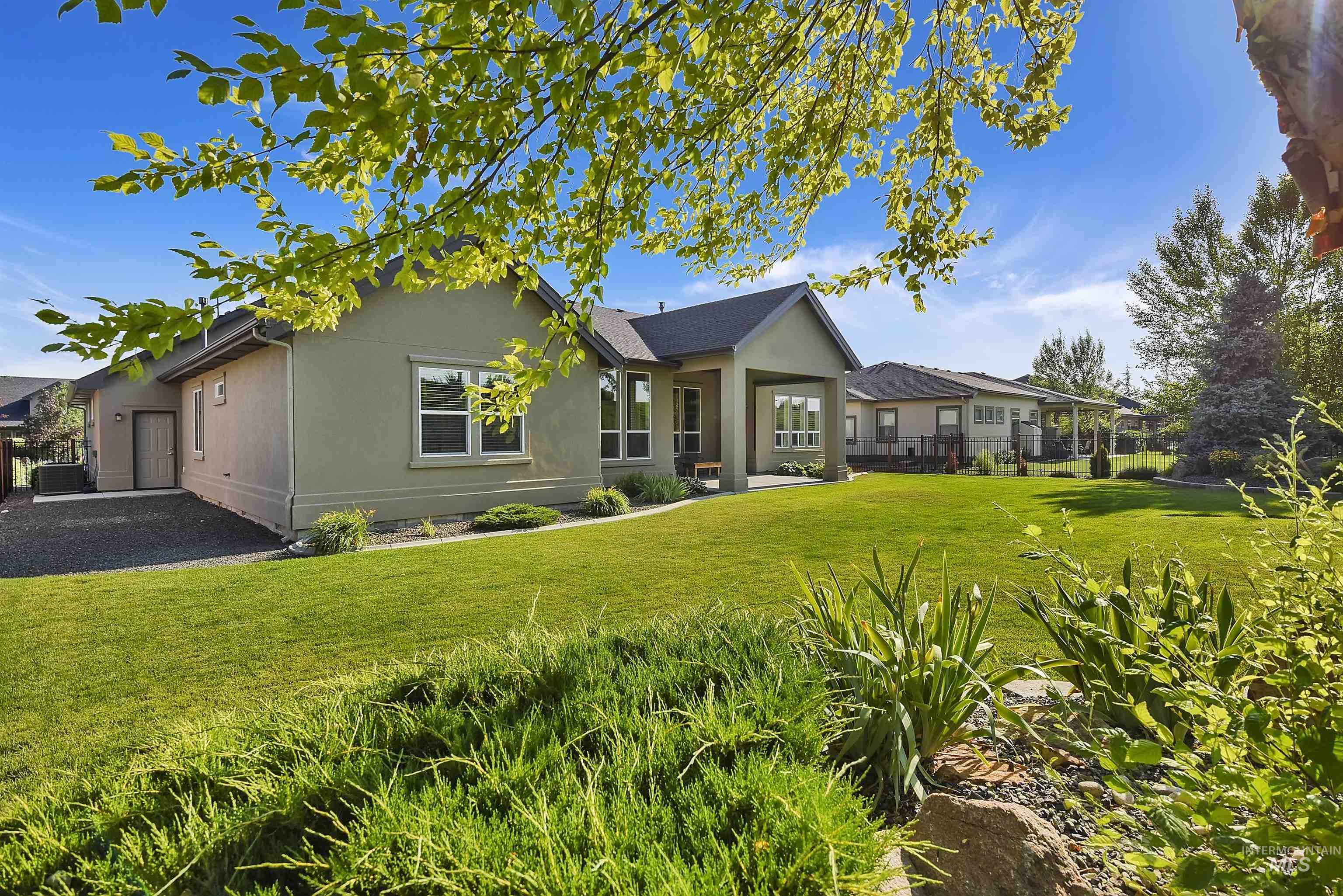 Expansive backyard featuring a manicured lawn, established landscaping, and a covered patio with recessed lighting