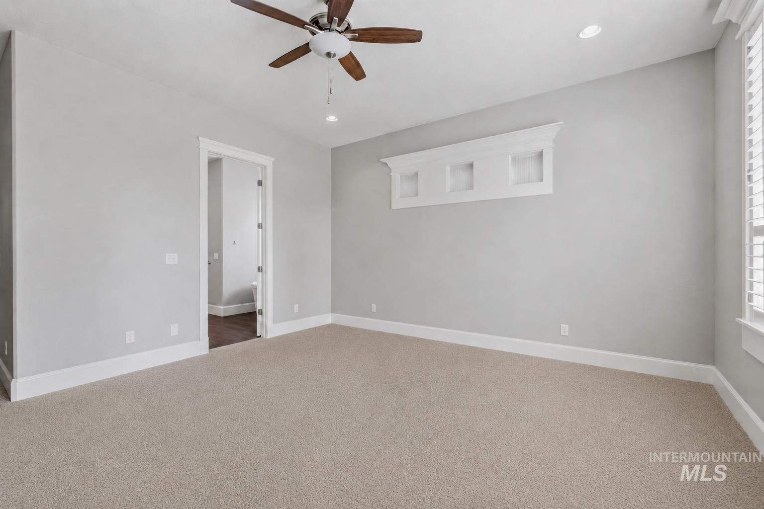 Carpeted interior room featuring light gray wall paint, white baseboards, and a ceiling fan with wood-finish blades