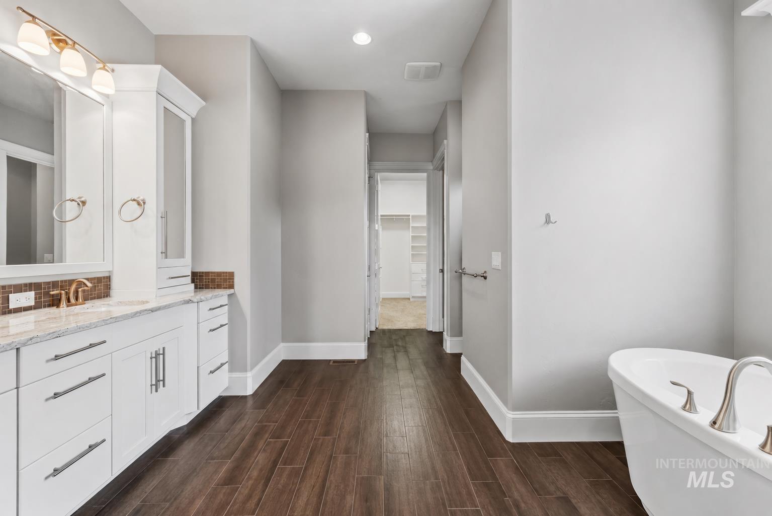 Bathroom featuring a freestanding soaking tub, dual vanity with granite countertop and bronze fixtures, built-in storage cabinetry, and wood-finish tile flooring
