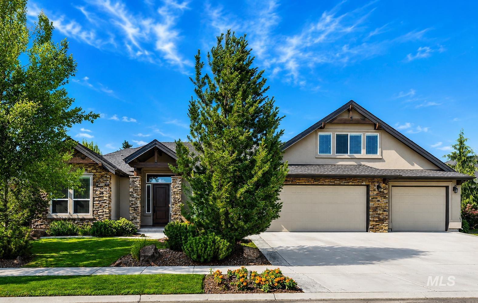 Stucco and stone facade with a three-car garage, mature landscaping, a prominent front entry, and multiple windows