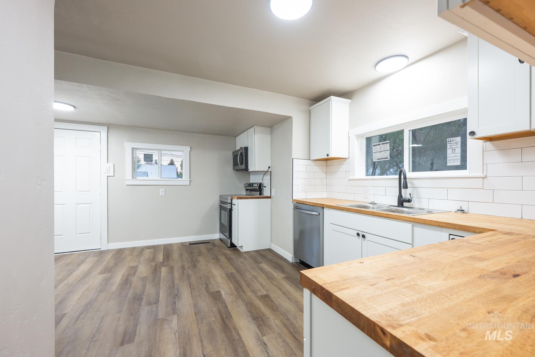 Kitchen featuring white cabinets, dark wood-type flooring, butcher block countertops, decorative backsplash, and appliances with stainless steel finishes