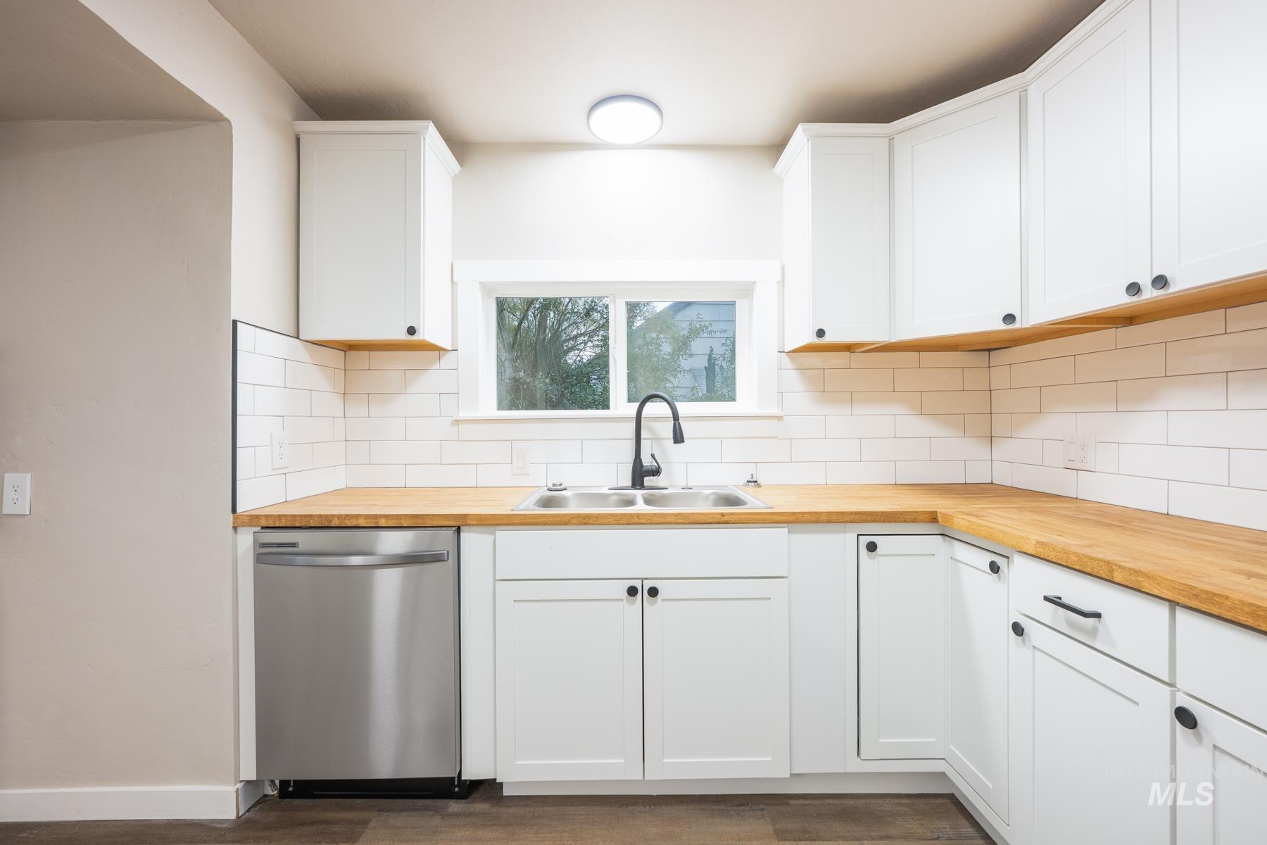 Kitchen featuring stainless steel dishwasher, white cabinets, and wood counters