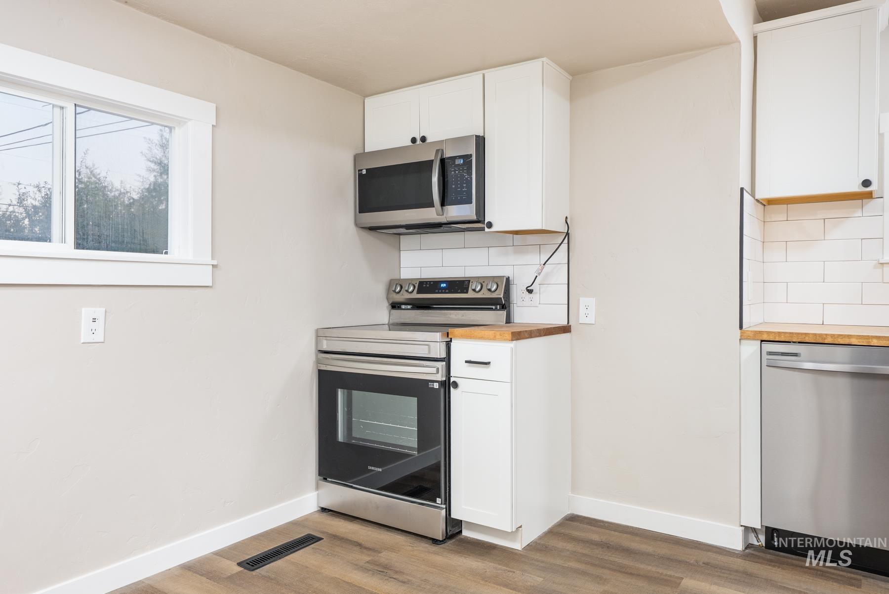 Kitchen featuring white cabinetry, appliances with stainless steel finishes, butcher block countertops, backsplash, and light wood-style flooring