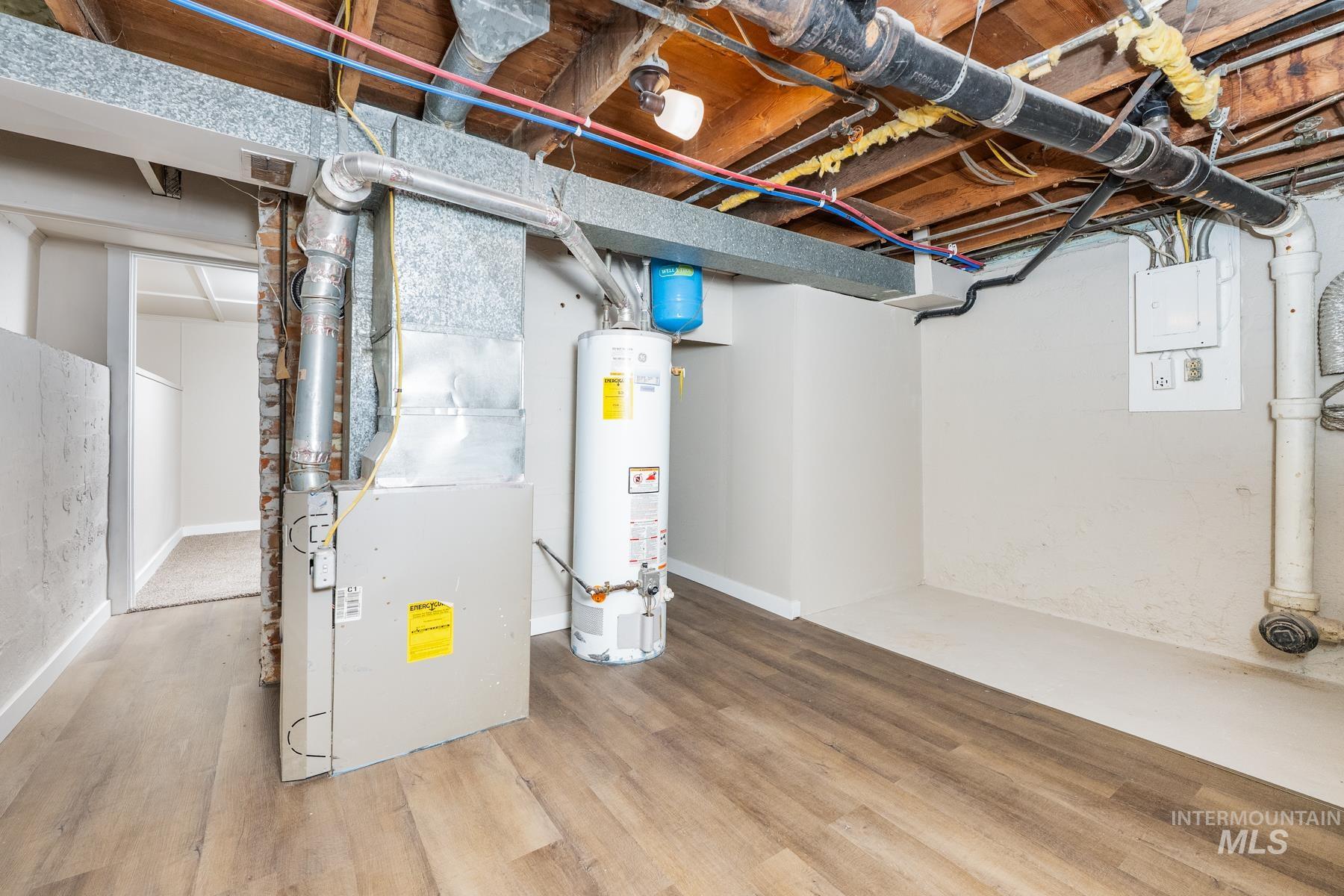 Unfinished basement with heating unit, gas water heater, and wood finished floors