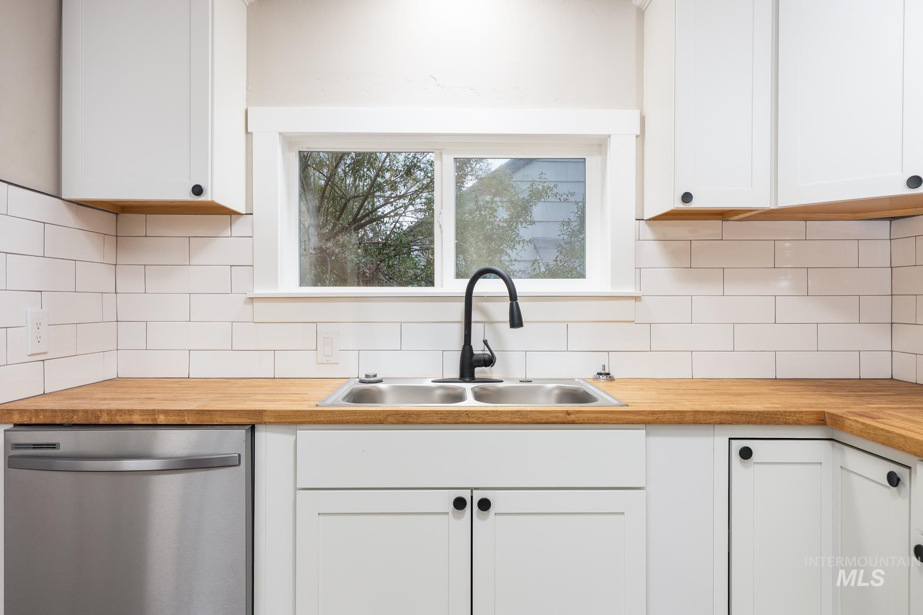 Kitchen with stainless steel dishwasher, white cabinetry, and tasteful backsplash