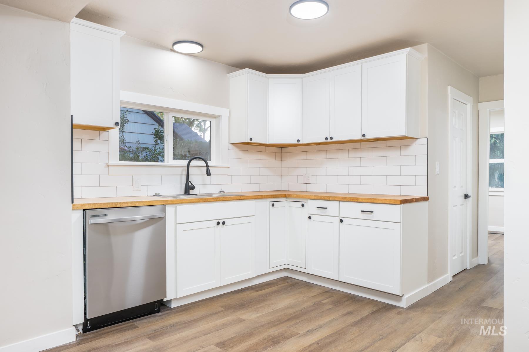 Kitchen featuring butcher block countertops, dishwasher, white cabinets, and light wood-style floors