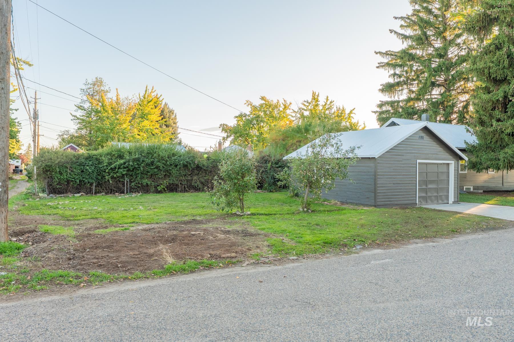 View of green lawn featuring an outdoor structure, a garage, and driveway