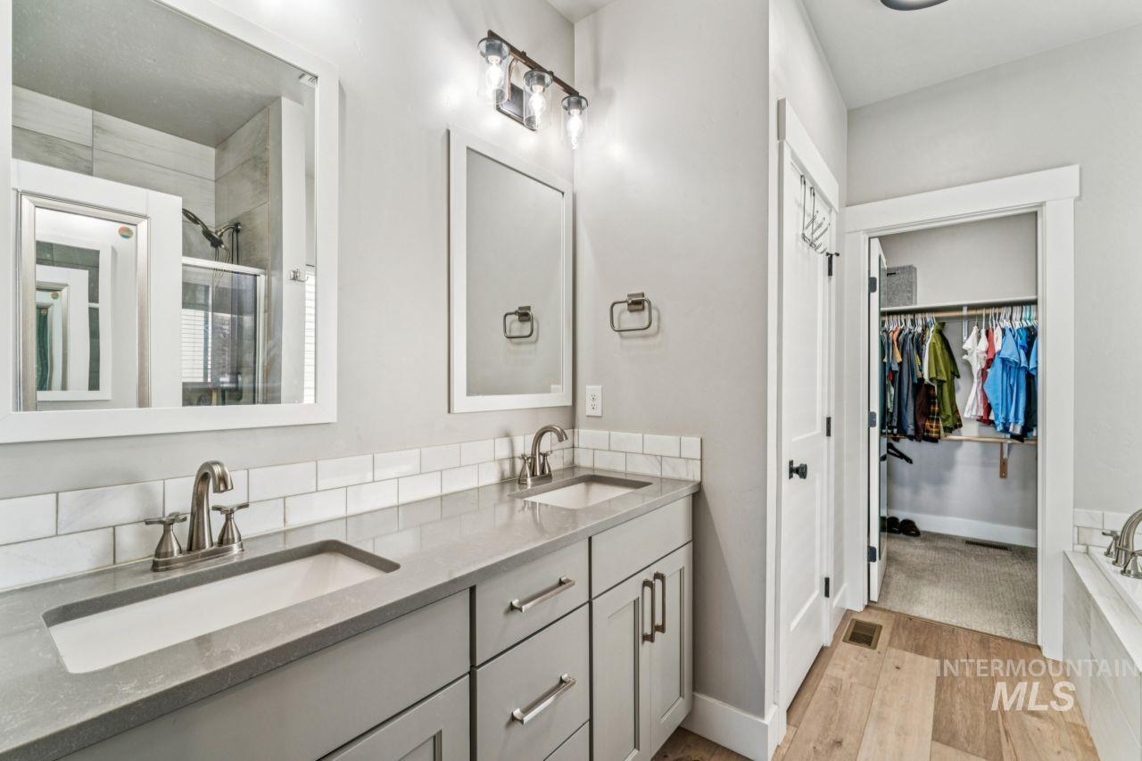 Bathroom featuring double vanity, a shower stall, light wood-style floors, a walk in closet, and a garden tub