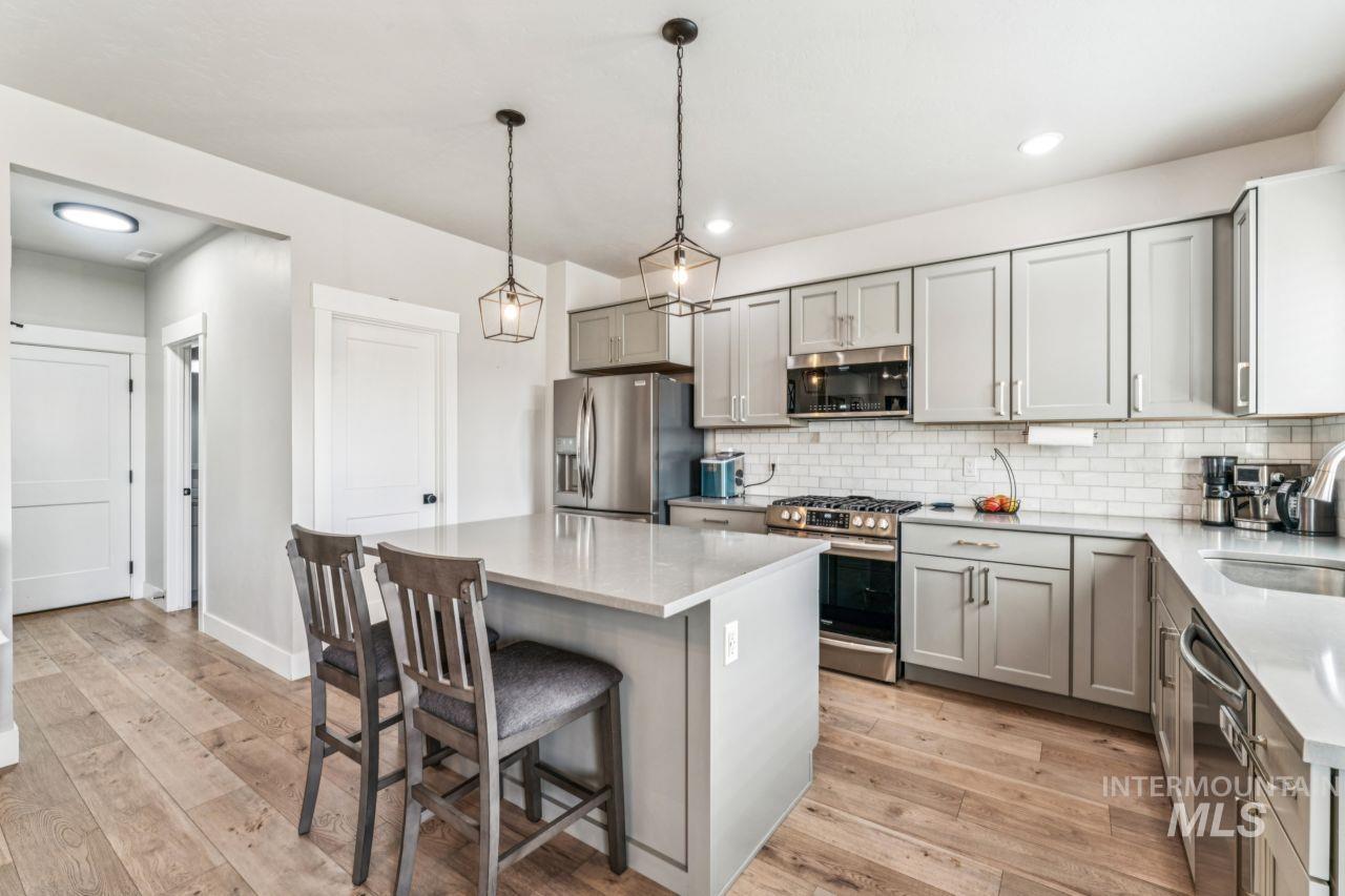 Kitchen featuring gray cabinetry, appliances with stainless steel finishes, light stone countertops, decorative backsplash, and a center island